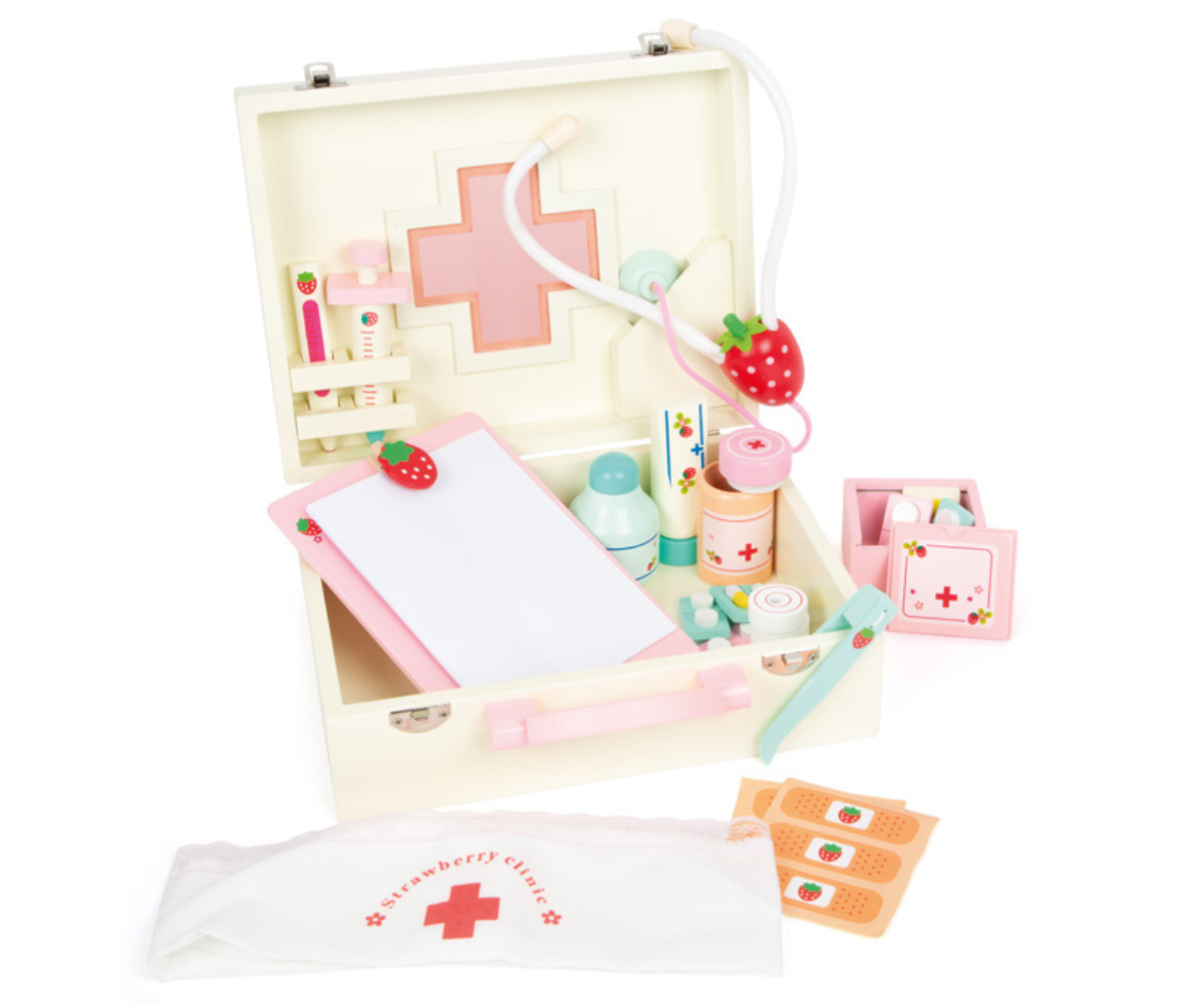 Õrnroosa puidust arstimängu kohver koos tarvikutega laotuna lauale.