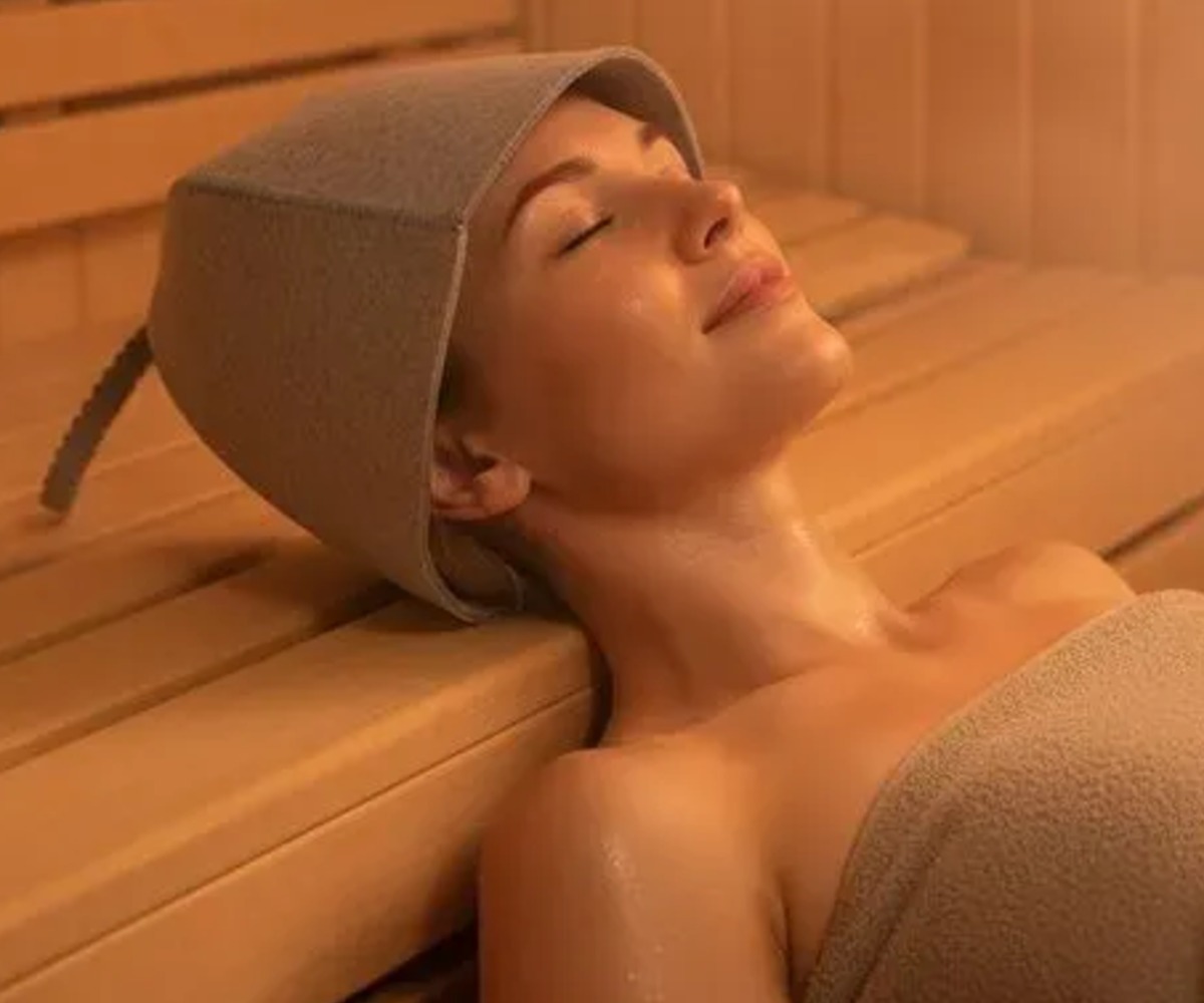 Naine lõõgastub saunas, kandes Saunamütsi ISOMEDIX vildist universaalne – hall.