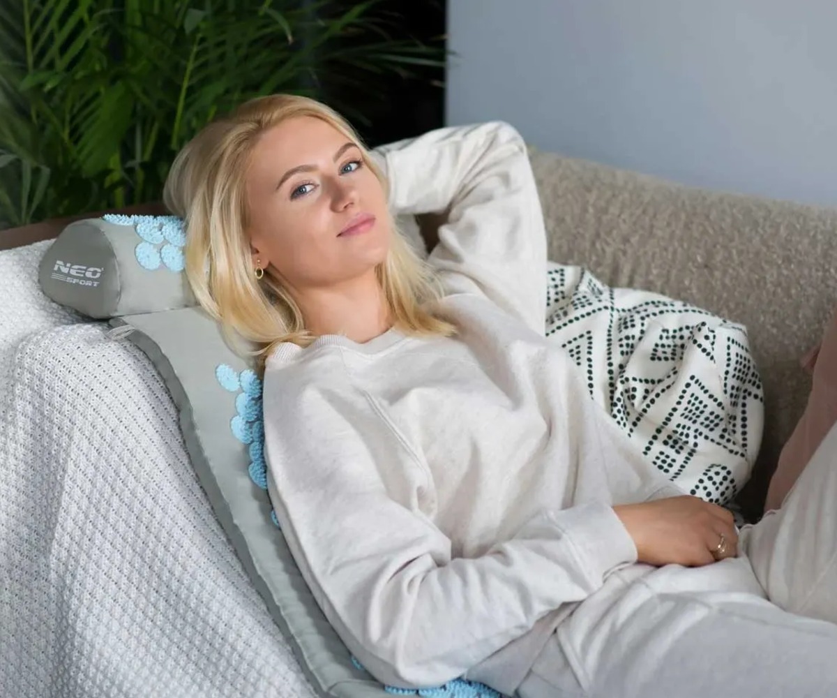 Naissoost inimene lõõgastumas akupressuurimatti padjaga Neo-Sport NS-901 – hall/sinine peal.
